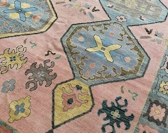 May include: A pink rug with a geometric pattern in shades of blue, yellow, and brown. The rug has a traditional design with intricate details.