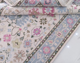 May include: A detailed shot of a rolled-up area rug with a floral pattern. The rug features a cream-colored background with blue, pink, and green floral designs. The border has a blue and cream pattern. The rug is made of a soft material.