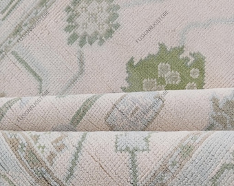 Könnte beinhalten: Nahaufnahme eines aufgerollten Teppichs mit floralem Muster. Der Teppich hat einen cremefarbenen Hintergrund mit grünen und hellblauen floralen und geometrischen Designs. Die Textur des Teppichs ist sichtbar und zeigt eine weiche, gewebte Konstruktion.