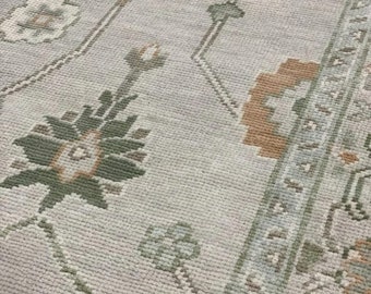 May include: A close-up of a light gray rug with a repeating pattern of green and brown floral designs. The rug has a soft, textured surface.