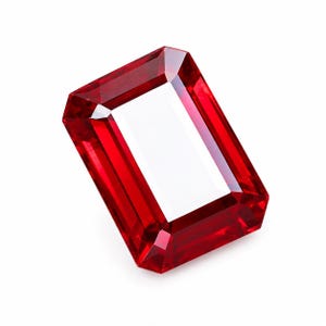 Könnte beinhalten: Ein leuchtend tiefroter Edelstein im rechteckigen Smaragdschliff. Der Stein weist präzise, facettierte Kanten auf, die das Licht reflektieren und ein klares, transparentes Zentrum sowie gesättigte karmesinrote Farbtöne erzeugen.