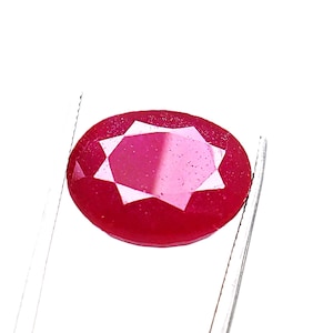 May include: A deep red oval-shaped gemstone with a star-shaped facet pattern.