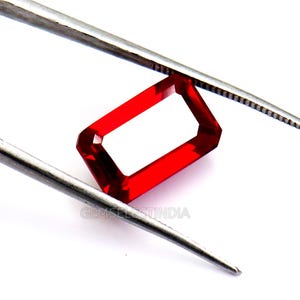 May include: A rectangular, faceted red gemstone is held by silver tweezers against a white backdrop. The gemstone has a hollow centre and is a vibrant, transparent red colour. The text "GEMSELECTINDIA" is visible.