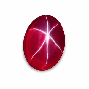 May include: An oval-shaped ruby gemstone displaying a six-rayed star effect. The deep red gem has bright white lines radiating from the centre, forming a starburst pattern. The stone is set against a white background.
