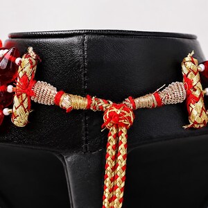 May include: A multi-strand necklace featuring deep red, teardrop-shaped glass beads accented with small white beads. The necklace includes gold-toned metallic cylindrical connectors and a braided red and gold cord closure with an adjustable knot.