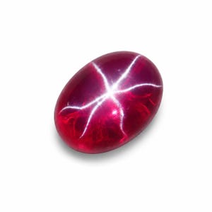 May include: Oval-shaped, polished ruby gemstone with a six-rayed star effect. The gem is a deep red colour with a bright white star pattern radiating from the centre. The gemstone is set against a white background.