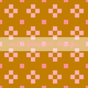 May include: A repeating pattern of pink crosses and squares on a golden-brown background. The text "wild blossom design" is displayed in a light pink font across the center of the image. This design is suitable for fabric, wallpaper, or digital art.