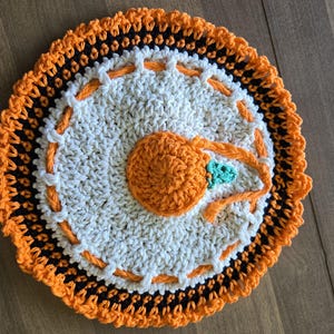 May include: A crocheted orange and black round coaster with a white centre and a smaller orange crocheted circle in the centre.