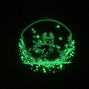 May include: A glow-in-the-dark wall hanging featuring a silhouette of a knight with a cape, surrounded by a swirling pattern of glowing green dots and lines.