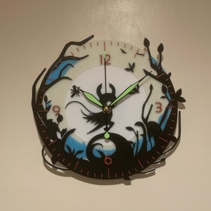 May include: Black and white clock featuring a silhouette of a creature with wings and a crown. The clock face is white with black numbers and hands. The background is a blue and white gradient.