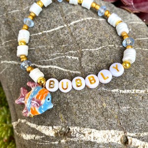 Pulsera Bubbly: Pulsera veraniega con peces de porcelana, arcilla polimérica y cuentas acrílicas, detalles dorados, hecha a mano y elástica.