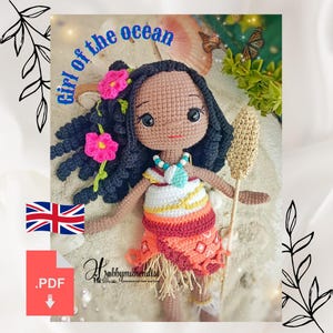 May include: A crocheted doll with dark skin, black hair, and pink flower accents. The doll wears a colorful dress and holds a staff. The text "Girl of the Ocean" is visible above the doll.