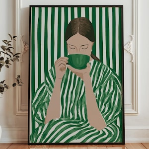 May include: An art print featuring a person sipping from a green cup. The person is wearing a green and white striped robe, set against a green and white striped background. The artwork is framed in a black frame.