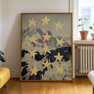 May include: A rectangular framed wall art piece featuring a black and white photographic print of a mountain range overlaid with several pale yellow, five-pointed star shapes. Some stars include small accents of bright pink along their edges.