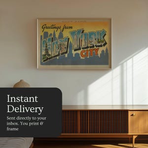 May include: Framed vintage-style postcard print with the text "Greetings from New York City." The print features a skyline illustration in blue, orange, and green hues. The framed print is displayed on a white wall above a wooden cabinet.
