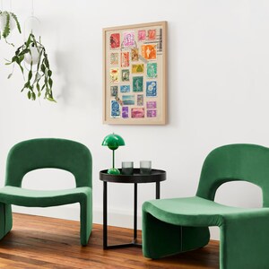 May include: Two green velvet chairs with a black side table in between. The table has a green lamp with a white shade on it. A framed picture of colorful stamps is on the wall behind the table.