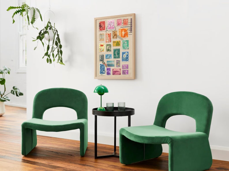 May include: Two green velvet chairs with a black side table in between. The table has a green lamp with a white shade on it. A framed picture of colorful stamps is on the wall behind the table.