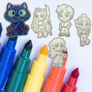 May include: A collection of colorful markers with black tips and a variety of colors, including blue, green, yellow, orange, and red. Several embroidered patches of cartoon characters and a blue cat are arranged on a white surface.