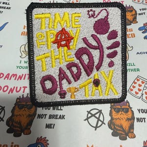 May include: A square embroidered patch with a white background and a black border. The text reads "TIME TO PAY THE DADDY TAX" in yellow and purple thread. It features a red anarchy symbol, a purple bomb icon, and a small gold trophy icon.