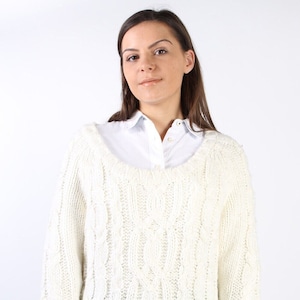 May include: A white cable knit jumper with a round neckline. The jumper is made from a soft, chunky yarn and has a relaxed fit.