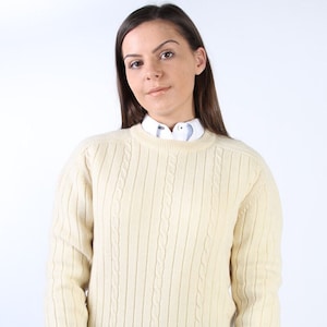 Könnte beinhalten: Ein cremefarbener Pullover mit Zopfmuster und Rundhalsausschnitt.