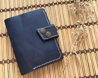 May include: A dark blue leather wallet with a flap closure and a stitched design. The wallet has two metal snaps and the text "WO Leather" is embossed on the front.