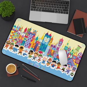 May include: A rectangular desk mat featuring a colorful graphic print of the Disney It's a Small World attraction. The design displays stylized buildings and a line of diverse cartoon characters against a light yellow and blue background.
