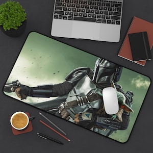 Op de afbeelding: Rechthoekige bureaumat met een gedetailleerde afbeelding van The Mandalorian met een blaster en Grogu. De achtergrond is een groene, bewolkte lucht. Een witte computermuis ligt op de mat.