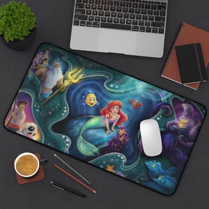 May include: A rectangular mousepad featuring a colorful illustration of characters from The Little Mermaid. The design includes Ariel, Flounder, Sebastian, King Triton, and Ursula, set against an underwater background with a laptop and accessories.