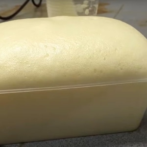 Pode incluir: Um recipiente retangular de pl&aacute;stico branco sujo preenchido com uma subst&acirc;ncia espumosa amarelo claro. A espuma est&aacute; a transbordar do recipiente, criando um topo arredondado. O recipiente est&aacute; sobre uma superf&iacute;cie.