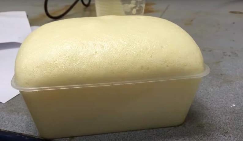 Pode incluir: Um recipiente retangular de pl&aacute;stico branco sujo preenchido com uma subst&acirc;ncia espumosa amarelo claro. A espuma est&aacute; a transbordar do recipiente, criando um topo arredondado. O recipiente est&aacute; sobre uma superf&iacute;cie.
