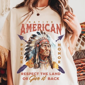 Puede incluir: Camiseta color crema con un diseño nativo americano. El diseño incluye las palabras "Native American Pride Honor" y "Respect the Land or Give it Back" alrededor de un retrato de un jefe nativo americano con un tocado.