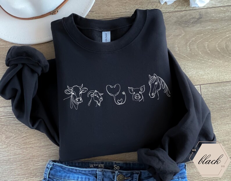 Op de afbeelding: Zwart sweatshirt met een witte omtrek van een koe, geit, stethoscoop, varken en paard. Het ontwerp is gecentreerd op de voorkant van het sweatshirt.