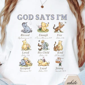 Könnte beinhalten: Weißes T-Shirt mit dem Text "GOD SAYS I'M" über neun Illustrationen von Winnie-Puuh-Charakteren. Jede Illustration hat ein zugehöriges Wort wie "Blessed" und einen Bibelvers. Das Wort "white" befindet sich in einem Sechseck.