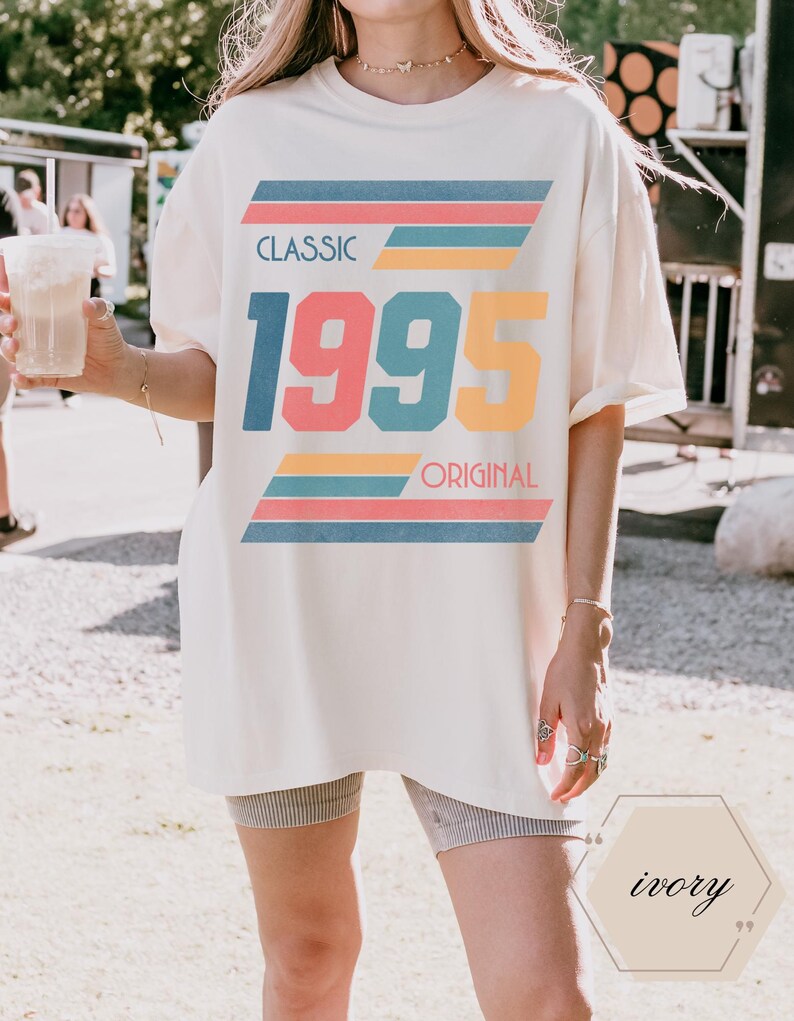 May include: A white oversized t-shirt with a retro graphic design featuring the text "CLASSIC 1995 ORIGINAL" in colorful block letters with stripes.