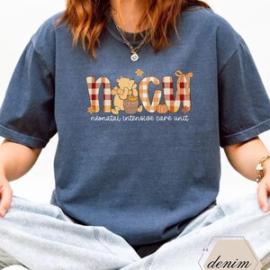 May include: A navy blue t-shirt with the letters "NICU" in a plaid pattern, with a Winnie the Pooh graphic. The text "neonatal intensive care unit" is below the letters. The shirt is a relaxed fit.