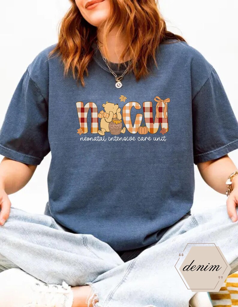 May include: A navy blue t-shirt with the letters "NICU" in a plaid pattern, with a Winnie the Pooh graphic. The text "neonatal intensive care unit" is below the letters. The shirt is a relaxed fit.