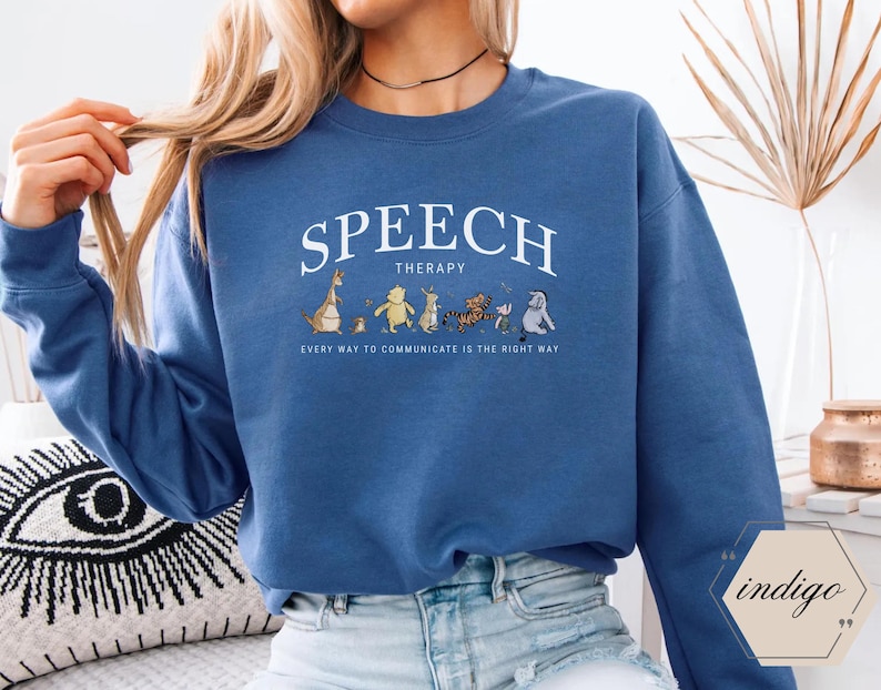 May include: Blue sweatshirt with the words "SPEECH THERAPY" in white arched text above a line of cartoon characters. Below the text is the phrase "EVERY WAY TO COMMUNICATE IS THE RIGHT WAY".