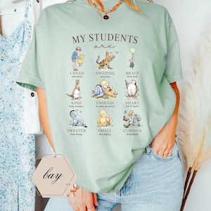 May include: A light green t-shirt with the text "MY STUDENTS are" and illustrations of Winnie the Pooh characters. The shirt also has the word "bay" in a hexagon shape.