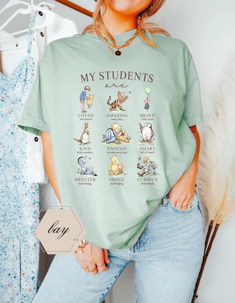 May include: A light green t-shirt with the text "MY STUDENTS are" and illustrations of Winnie the Pooh characters. The shirt also has the word "bay" in a hexagon shape.