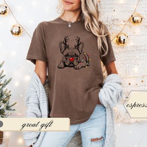 May include: Brown t-shirt featuring a graphic of a French Bulldog with reindeer antlers and a red nose. The dog is adorned with Christmas lights. The text "great gift" is displayed on a banner below the shirt.