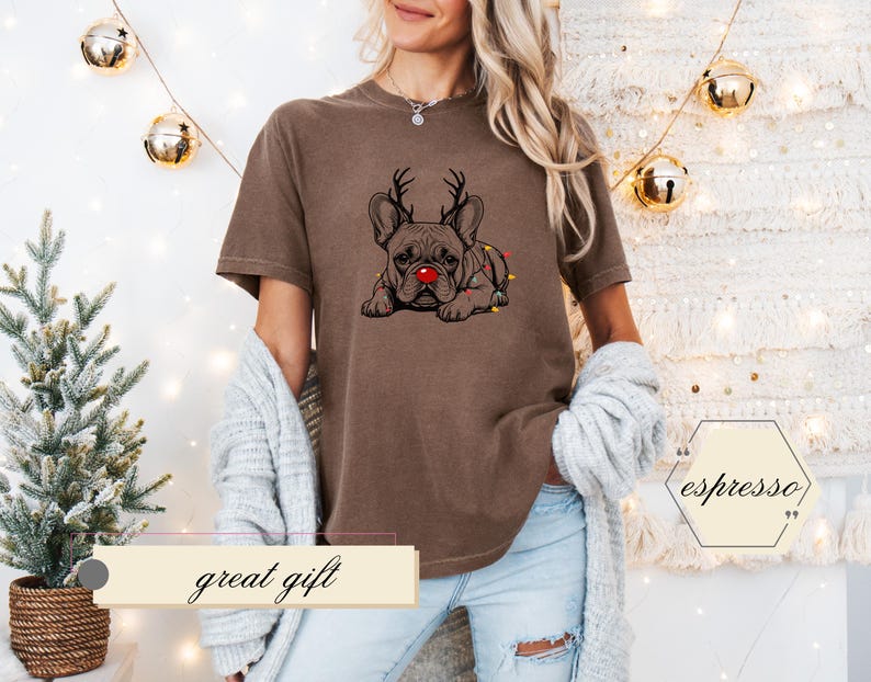 May include: Brown t-shirt featuring a graphic of a French Bulldog with reindeer antlers and a red nose. The dog is adorned with Christmas lights. The text "great gift" is displayed on a banner below the shirt.