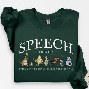 May include: Forest green sweatshirt with the words "SPEECH THERAPY" in white arched text above a line of cartoon characters. Below the text is the phrase "EVERY WAY TO COMMUNICATE IS THE RIGHT WAY".