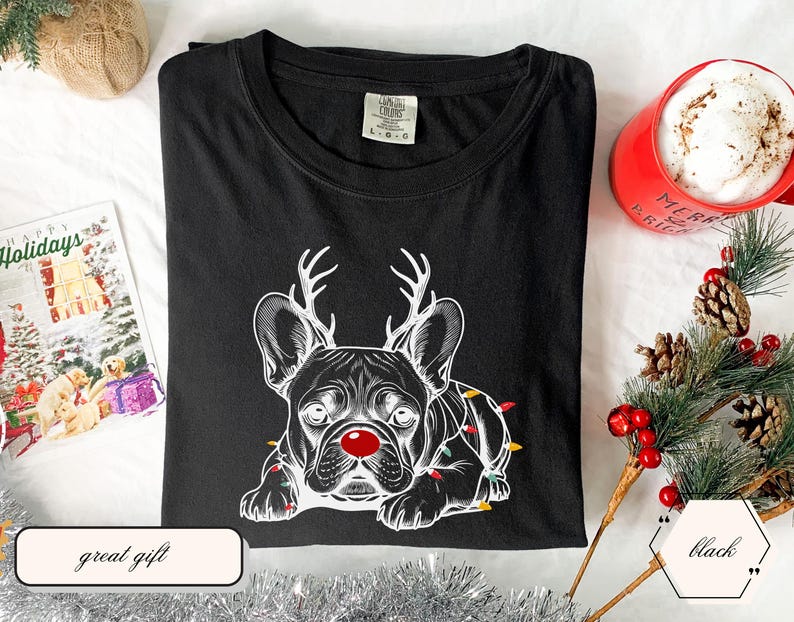 May include: Black t-shirt featuring a white graphic of a French Bulldog wearing reindeer antlers and a red nose, with Christmas lights. The shirt is part of a holiday collection and is a great gift.