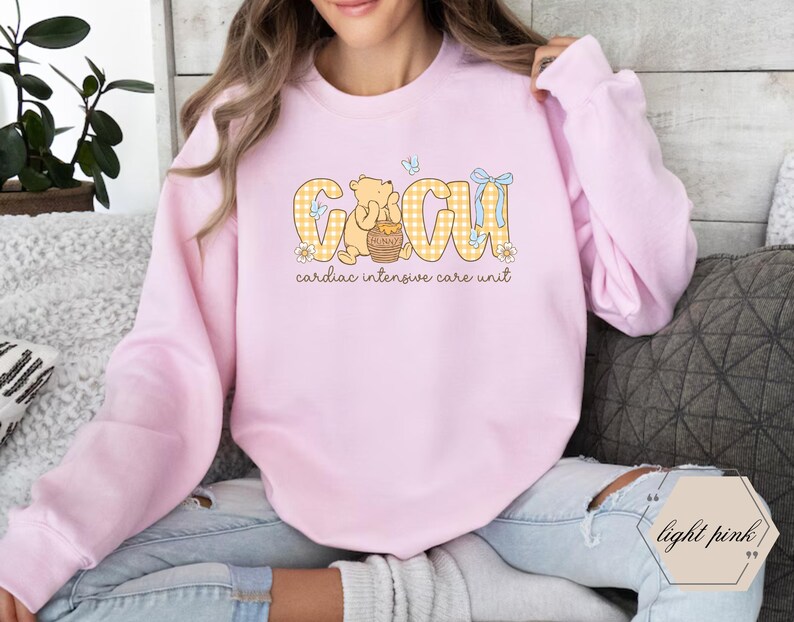 May include: Pale pink sweatshirt with "CICU" in yellow gingham, a cartoon bear, and "cardiac intensive care unit". The sweatshirt is made of a soft, comfortable material.