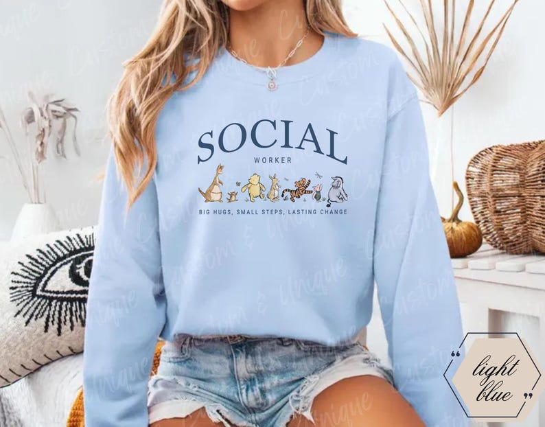 Pu&ograve; includere: Felpa azzurra con la scritta "SOCIAL WORKER" in blu navy. Sotto il testo ci sono personaggi dei cartoni animati. &Egrave; presente anche la scritta "BIG HUGS, SMALL STEPS, LASTING CHANGE".