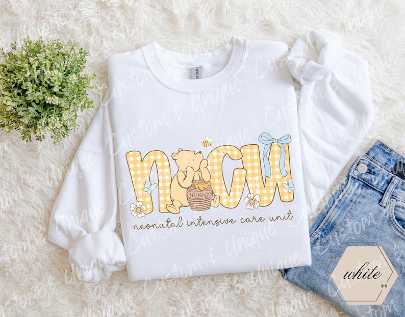 May include: White sweatshirt with the letters NICU in yellow gingham print, featuring a cartoon bear holding a honey pot. The text "neonatal intensive care unit" is below the letters. A blue bow and bee are also included.