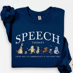 May include: Navy blue sweatshirt with the words "SPEECH THERAPY" in white arched text. Below the text is a line of cartoon characters. The phrase "EVERY WAY TO COMMUNICATE IS THE RIGHT WAY" is printed below the characters.