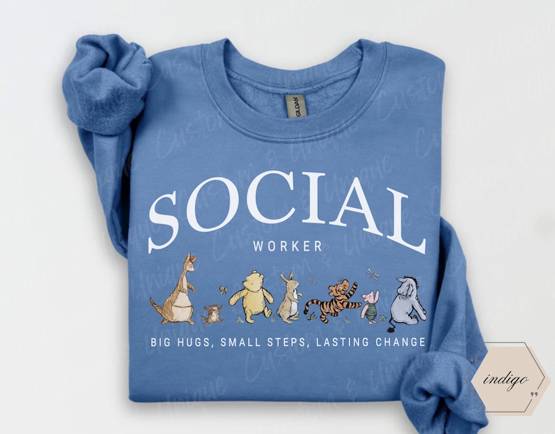 Pu&ograve; includere: Una felpa blu chiaro con la scritta bianca "SOCIAL WORKER". Sotto, personaggi dei cartoni animati. La frase "BIG HUGS, SMALL STEPS, LASTING CHANGE" &egrave; stampata in basso. La felpa ha le maniche lunghe.