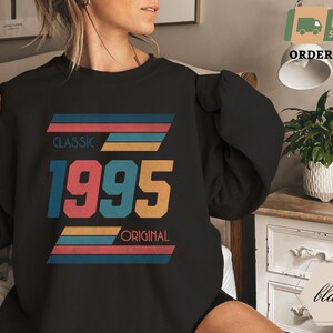 May include: Black sweatshirt with a vintage-style graphic design featuring the year 1995 with the words "Classic" and "Original" in colorful stripes.